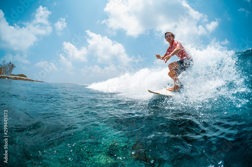 Young caucasian man surfs the ocean wave and makes a lot of splashes into the camera. Chickens surf spot in Maldives