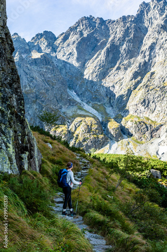 A woman (tourist) with trekking poles and a backpack on a trail in the mountains. Admiring the beautiful landscape in the morning. Tatra Mountains. Slovakia.