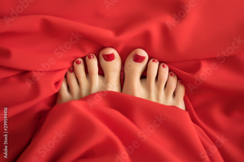 female fingers with red pedicure from under the red covers Close-up of covered female feet with red pedicure