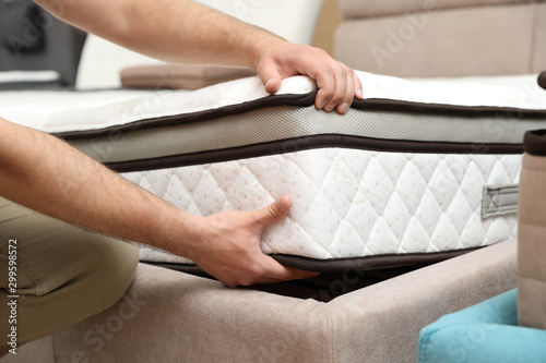 Young man choosing new orthopedic mattress in store, closeup