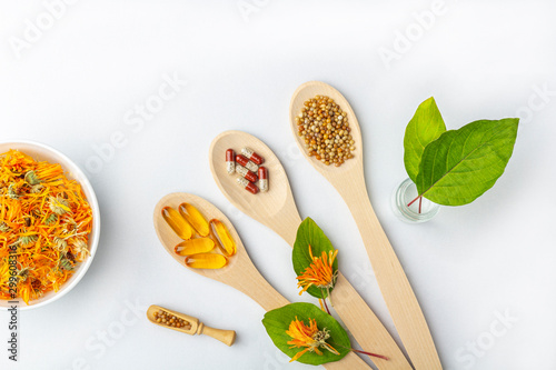 Herbal capsule, natural vitamins, dry leaves of calendula at wooden spoon on white background. Concept of healthcare and alternative medicine: homeopathy and naturopathy.