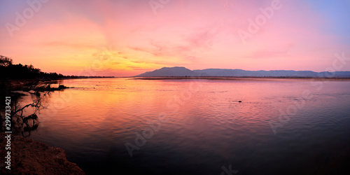 Panoramic view of sunset on the african Zambezi river. The dramatic, red sky reflects on the surface of the border river. View over the flood plain to the mountains on the Zambian side of the river.