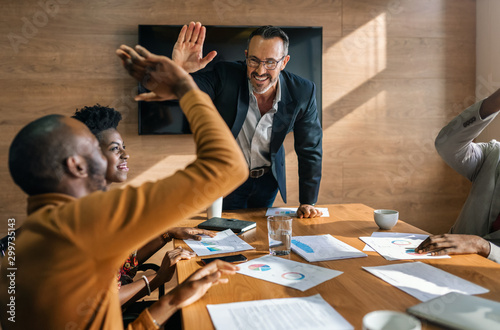 Two colleagues giving high five in meeting. Diverse business people celebrating success in boardroom.