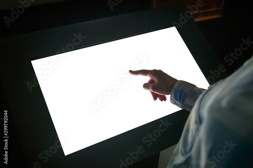 Woman hand using white blank interactive touchscreen display of electronic multimedia kiosk in dark room - scrolling and touching - close up view. Mock up, copyspace, template and technology concept