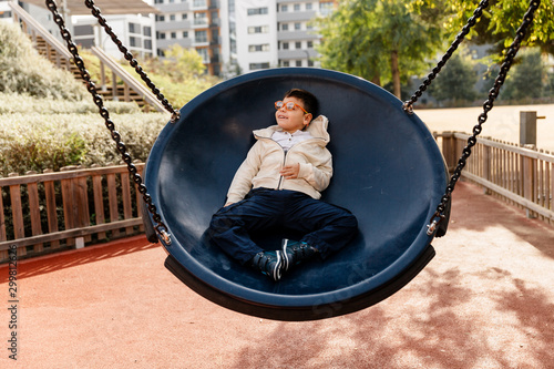 niño en el parque en columpio grande redondo balanceándose y riendo . Niño con pluri discapacidad.