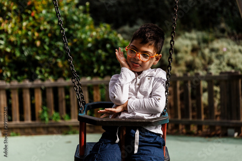 niño en columpio riendo haciendole cosquillas en parque. con discapacidad, con gafas.