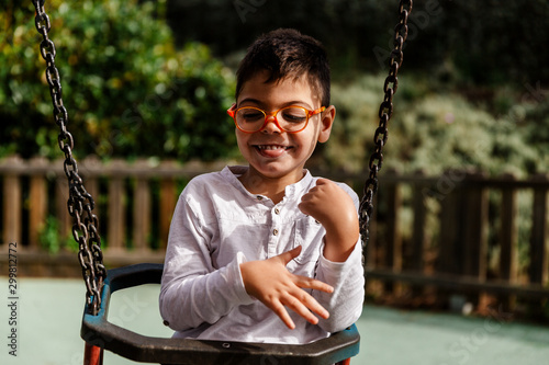 niño en columpio riendo haciendole cosquillas en parque. con discapacidad, con gafas.