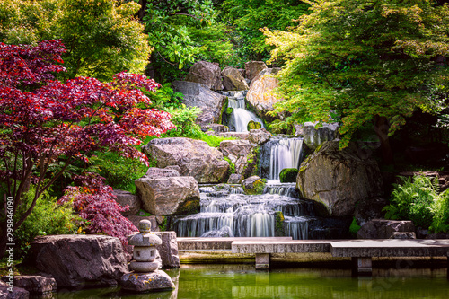 Waterfall long exposure with maple trees and bridge in Kyoto Japanese green Garden in Holland Park green summer zen lake pond water in London, UK