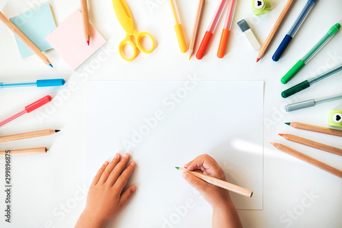 Close up of child's hands drawing at white paper within colorful pens and pencils.