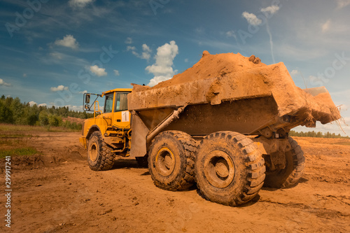 large yellow dirty dump truck with large wheels loaded with earth