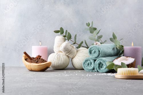 Beautiful spa and relax concept. Coffee with cinnamon scrub, cotton pouches with herbs for massage, sea stones, eucalyptus and other Spa accessories on grey table.