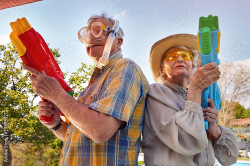 Modern Senior couple have fun playing with water gun.