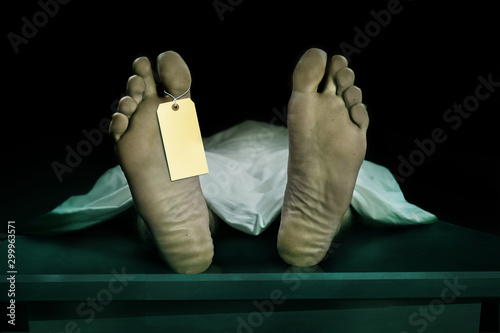 Male human body lying dead at morgue with blank identity label and covered with sheet . Close-up foot of man cadaver with identification toe tag in death concept