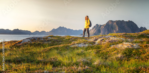 Woman with a backpack looks at the fjord. Ocean and mountain sunset landscape. Scenic view. Travel, adventure Explore North Norway. Summer in Scandinavia