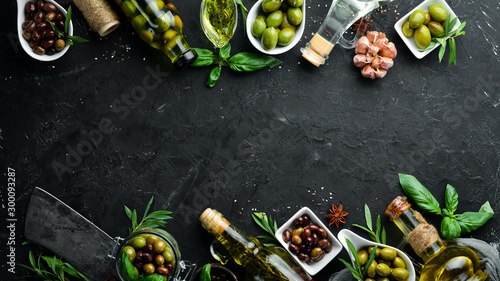 Olive oil, olives and spices on a black stone background. Top view. Free space for your text.