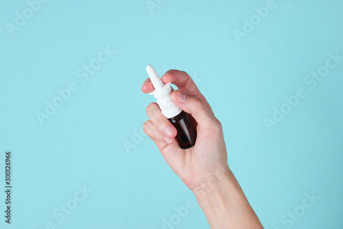 Female hand holds nasal spray on a blue background. Rhinitis treatment