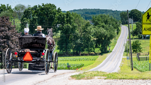 Amish Open Horse and Buggy with 2 Amish Adults in it trotting down the Hill on a Sunny Day