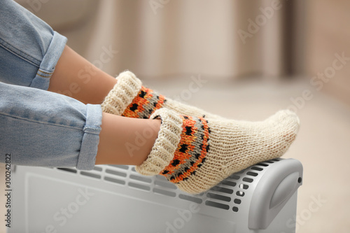 Woman warming feet on electric heater at home, closeup