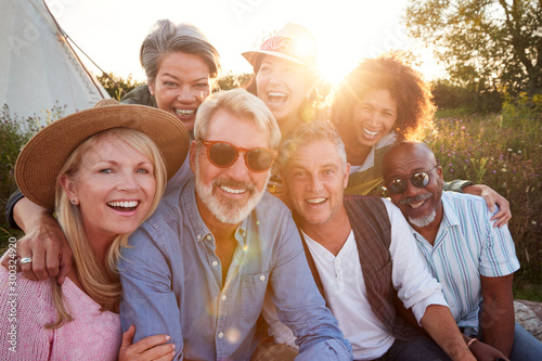 Portrait Of Mature Friends By Tent On Camping Vacation Against Setting Sun