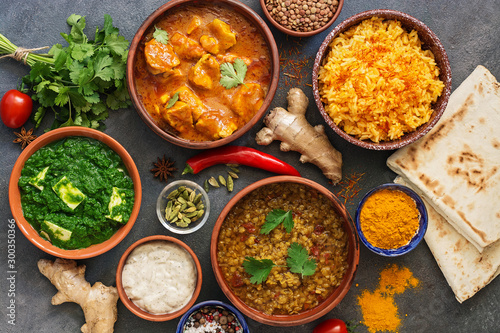 Assorted Indian food on a dark rustic background. Traditional Indian dish Chicken tikka masala, palak paneer, saffron rice, lentil soup, pita bread and spices. Top view, flat lay.