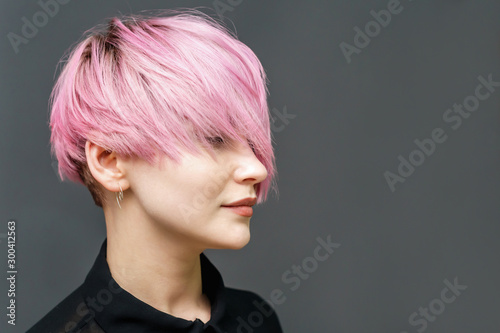 Portrait of adult girl with modern short pink hairstyle and closed eyes on the gray background with copy space.