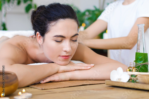 Young pleased woman is getting thai massage, therapy. Female hands of master are kneading back of client. Brunette girl is lying on couch in light spa ayurveda salon. Relax and health care concept.
