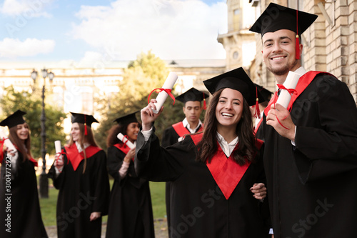 Happy students with diplomas outdoors. Graduation ceremony