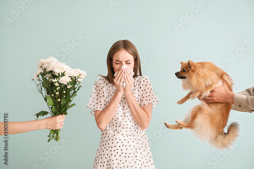 People giving flowers and dog to young woman suffering from allergy on light background