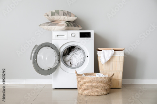 Modern washing machine with laundry near white wall