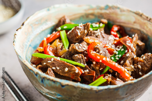 Asian teriyaki beef with green onions and sesame seeds in beautiful bowl, gray background.