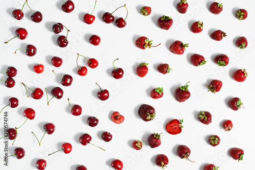 Berries of fresh ripe cherries and strawberries are scattered on a white surface. Top view.