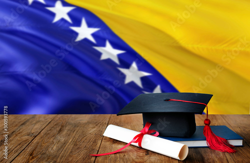 Bosnia Herzegovina education concept. Graduation cap and diploma on wooden table, national flag background. Succesful student.