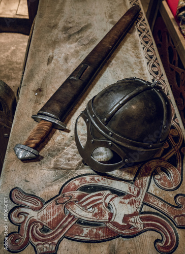 Viking helmet and viking sword on wooden table with wood carvings.