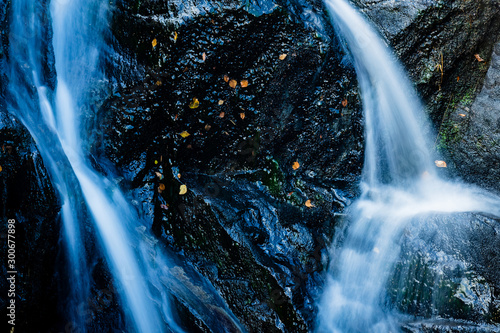 close up shot of a waterfall in the argyll region of the highlands of scotland in autumn showing bright water flowing over dark black rock