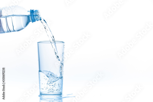 Pouring water from bottle into glass on white background. Photo with copy space.