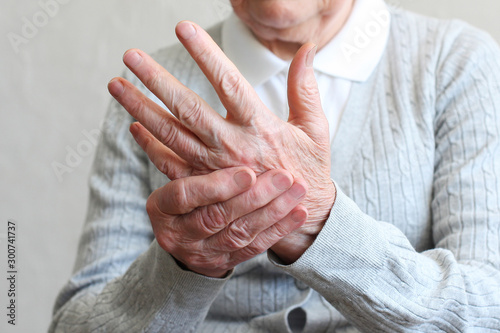 Elderly woman applying moisturizing lotion cream on hand palm, easing aches. Senior old lady experiencing severe arthritis rheumatics pains, massaging, warming up arm. Close up, copy space, background