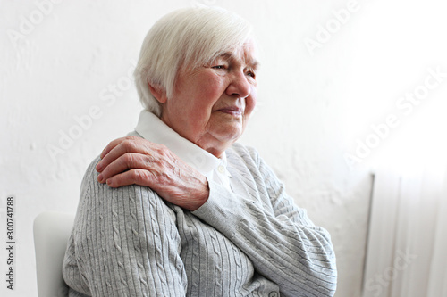 Elderly woman massaging the shoulder easing the aches. Joint pain concept. Senior old lady experiencing severe arthritis rheumatics pains, massaging, warming up arm. Close up, copy space, background