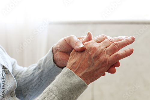 Elderly woman applying moisturizing lotion cream on hand palm, easing aches. Senior old lady experiencing severe arthritis rheumatics pains, massaging, warming up arm. Close up, copy space, background