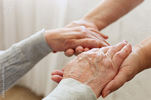 Mature female in elderly care facility gets help from hospital personnel nurse. Senior woman w/ aged wrinkled skin & care giver, hands close up. Grand mother everyday life. Background, copy space.