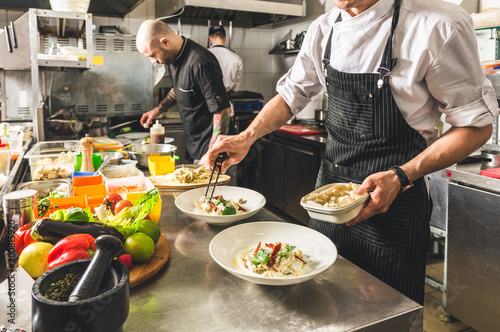 Professional chef cooking in the kitchen restaurant at the hotel, preparing dinner. A cook in an apron makes a salad of vegetables and pizza.