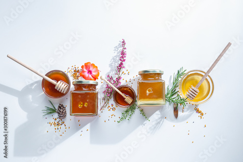 Composition of honey jars with honey sticks ,flowers and bee pollen on white background