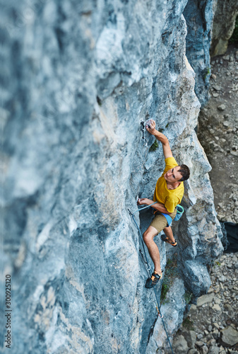 top view of man rock climber in yellow t-shirt, climbing on a cliff, searching, reaching and gripping hold, attaching rope. outdoors rock climbing and active lifestyle concept, 4K stock footage