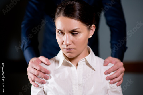 a man stands behind the girl and holds her by the shoulders, and the girl is unpleasant