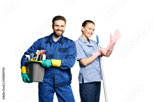 Attractive young woman and man in cleaning uniform and rubber gloves holding a mop and a bucket of cleaning products in his hands, isolated on white background.