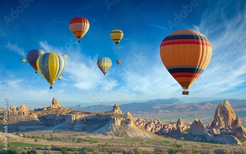 Colorful hot air balloons fly in blue sky over amazing valleys with fairy chimneys in Cappadocia, Turkey