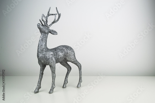 Silver glitter coated Reindeer Table Top Christmas ornament stood up on a white reflective surface.