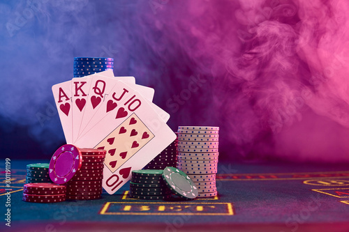 Winning combination in poker leaning on colored chips piles on blue cover of playing table. Black, smoke background, red and blue backlights. Casino.