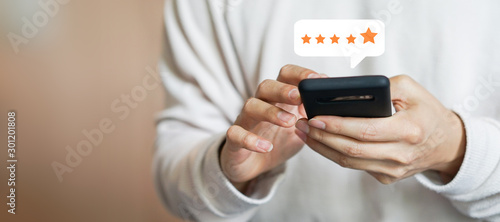 close up on customer man hand pressing on smartphone screen with gold five star rating feedback icon and press level three rank (good) for give score point to review the service business concept 