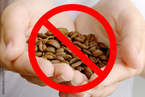 Danger and harm of caffeine. Red prohibitory sign on coffee beans in female hands