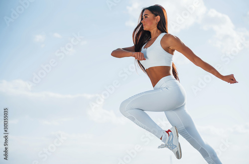 Up in the sky. Female runner in white sportive clothes doing fitness